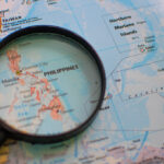 Detailed geographical map of the Philippines under a magnifying glass, illustrating the archipelagic nature of the country. A visual aid for discovering fascinating fun facts about the Philippines and its unique location in Southeast Asia.