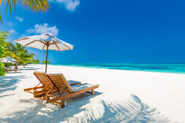 A beautiful tropical beach scene featuring two wooden lounge chairs and a white umbrella on pristine white sand, with palm leaves casting shadows, bright turquoise ocean water, and a clear blue sky, evoking the atmosphere of all inclusive resorts Philippines.