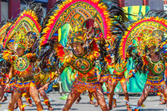 Performers in elaborate, colourful feathered costumes and headdresses dancing in a street parade at the Dinagyang Festival.