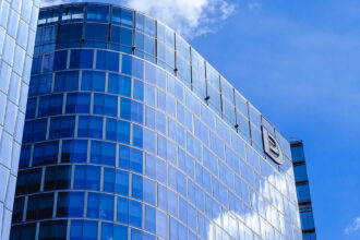 A modern, curved blue glass skyscraper in a financial district under a bright blue sky, reflecting clouds, showcasing the contemporary side of the city and suggesting that is Manila worth visiting.