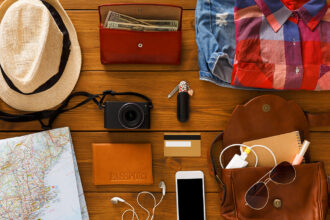 A flat lay of travel essentials packed on a wooden surface, including a hat, a map, a camera, a passport, a wallet with cash, credit cards, a smartphone, and a change of clothes, emphasising preparation and making it clear is Manila worth visiting.