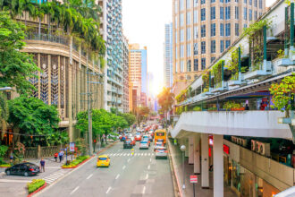 Wide, well-maintained street in Makati City, Metro Manila, flanked by lush tropical trees and upscale commercial buildings. This organized cityscape reflects the well-developed and secure nature of the area, providing evidence for those asking, is manila safe.