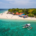 A sandy beach lined with local buildings and a boat in the clear turquoise water of Moalboal, Cebu, a popular Philippines scuba diving spot.