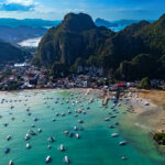 Aerial view of El Nido, Palawan, featuring a bay full of boats ready for island hopping Philippines beneath lush, towering limestone karsts.
