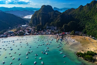 Aerial view of El Nido, Palawan, featuring a bay full of boats ready for island hopping Philippines beneath lush, towering limestone karsts.