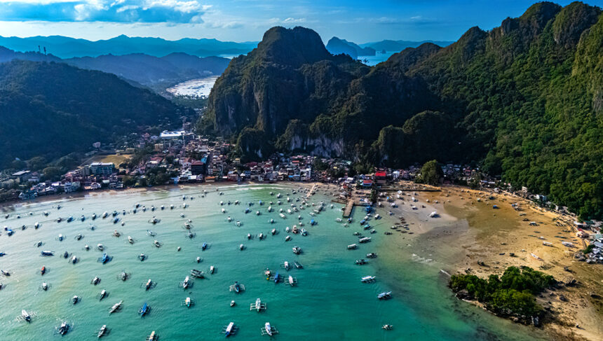 Aerial view of El Nido, Palawan, featuring a bay full of boats ready for island hopping Philippines beneath lush, towering limestone karsts.