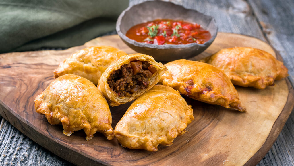 Traditional South American empanada de carne offered with a chili dip as closeup on a rustic wooden board- vigan tourist spots