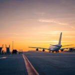 Wide shot of an airport runway glowing under a golden sunset, capturing the mood of travellers searching for the cheapest flight to the Philippines as planes move across the tarmac.