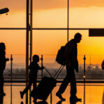 Silhouette of a family pulling luggage through an airport terminal at sunset, representing travellers beginning their journey after securing the cheapest flight to the Philippines.