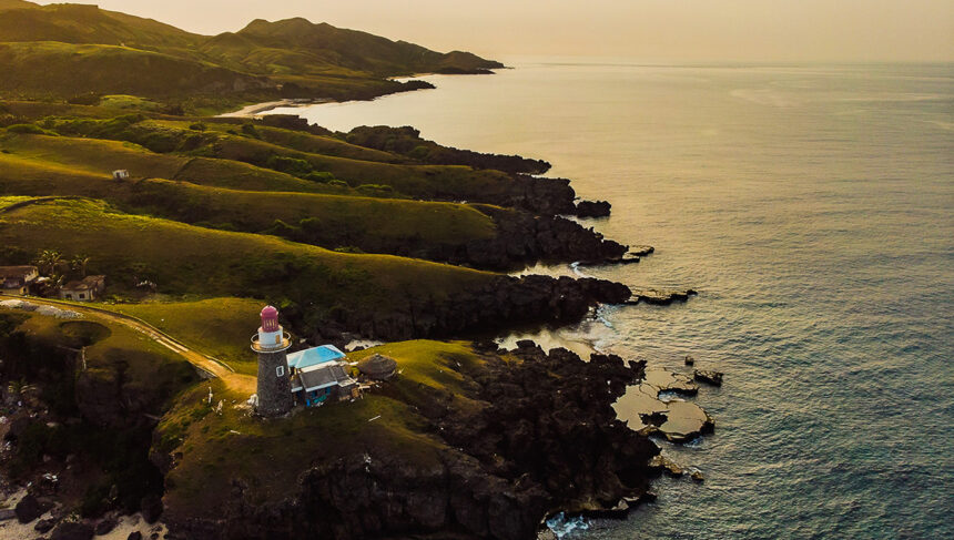 Batanes tourist attraction featuring green hills and beach at sunset in Batanes, Philippines