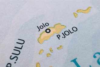 A close-up photograph of a printed map showing Jolo Island, labeled as "P. JOLO," with a black circle indicating the location of the town of Jolo within the Sulu Archipelago.