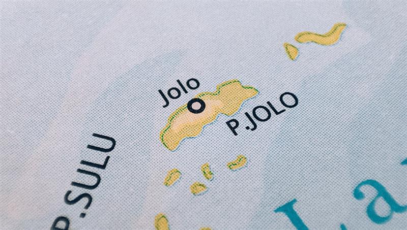 A close-up photograph of a printed map showing Jolo Island, labeled as "P. JOLO," with a black circle indicating the location of the town of Jolo within the Sulu Archipelago.