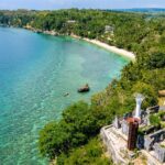 A panoramic view from the historical Guisi Lighthouse ruins on a cliff, overlooking the turquoise waters and coral reefs of Guisi Beach, a popular destination for things to do in Guimaras.