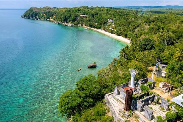 A panoramic view from the historical Guisi Lighthouse ruins on a cliff, overlooking the turquoise waters and coral reefs of Guisi Beach, a popular destination for things to do in Guimaras.
