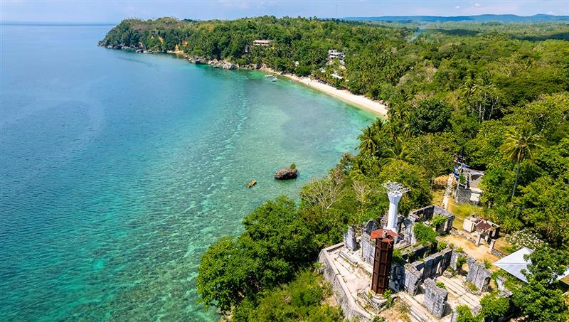 A panoramic view from the historical Guisi Lighthouse ruins on a cliff, overlooking the turquoise waters and coral reefs of Guisi Beach, a popular destination for things to do in Guimaras.