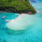 Aerial view of Paliton Beach in Siquijor showing a white sandbar, outrigger boats, and crystal-clear turquoise water under a lush green canopy.