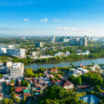 An aerial high-angle view of the Iloilo City skyline featuring the Iloilo River snaking through the cityscape, with modern high-rise buildings and residential areas under a clear blue sky—a perfect starting point for travelers looking for things to do in Iloilo City.