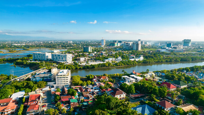 An aerial high-angle view of the Iloilo City skyline featuring the Iloilo River snaking through the cityscape, with modern high-rise buildings and residential areas under a clear blue sky—a perfect starting point for travelers looking for things to do in Iloilo City.