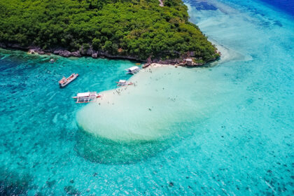 Aerial view of Paliton Beach in Siquijor showing a white sandbar, outrigger boats, and crystal-clear turquoise water under a lush green canopy.