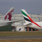An Emirates Airbus A380 and a Qatar Airways Boeing 777 taxiing on the runway at Manchester Airport. A comparison of Qatar Airways vs Emirates aircraft side-by-side on a clear day.