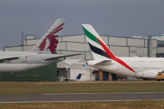 An Emirates Airbus A380 and a Qatar Airways Boeing 777 taxiing on the runway at Manchester Airport. A comparison of Qatar Airways vs Emirates aircraft side-by-side on a clear day.