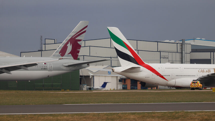 An Emirates Airbus A380 and a Qatar Airways Boeing 777 taxiing on the runway at Manchester Airport. A comparison of Qatar Airways vs Emirates aircraft side-by-side on a clear day.