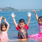 Local children playing in the turquoise shallows of a tropical beach, enjoying the bright sunshine and clear skies of the Philippines weather in March.