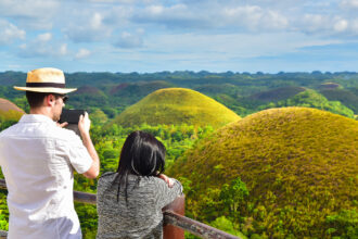 Tourists at a viewpoint overlooking the lush green Chocolate Hills in Bohol, a popular destination during the sunny intervals of Philippines weather May.