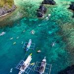 Aerial view of outrigger boats and kayakers in a turquoise lagoon, a popular stop when spending 2 weeks in Philippines exploring Palawan.