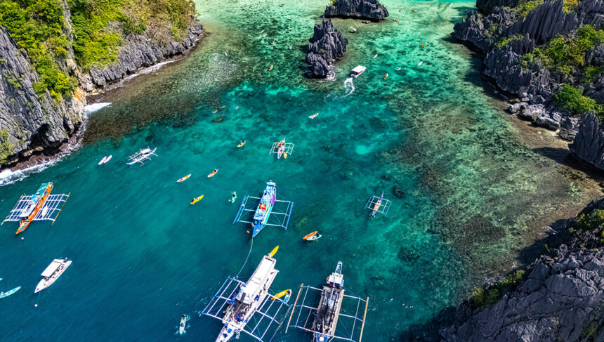 Aerial view of outrigger boats and kayakers in a turquoise lagoon, a popular stop when spending 2 weeks in Philippines exploring Palawan.